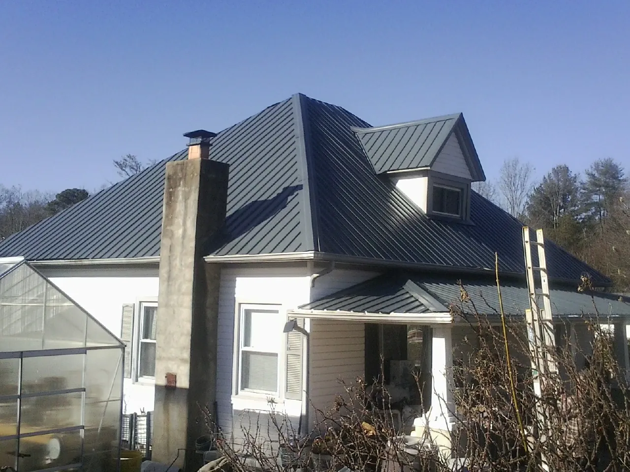 Dark blue standing seam metal roof on a white farmhouse with dormer — Slate & Tile Roof Repair by Roofing Brothers in Laughlintown