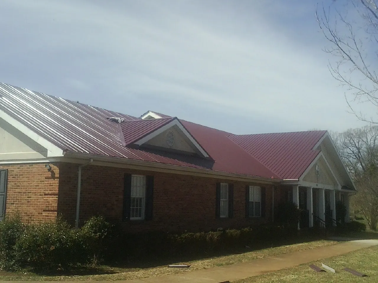 Red metal roof with gabled entries on a long brick building, from a Hail Damage Roof Repair job in Laughlintown