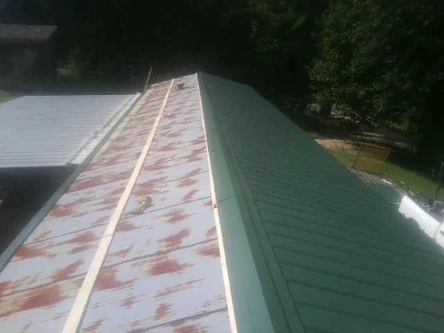 Old rusted panels beside newly installed green metal roofing — Wind Damage Roof Repair by Roofing Brothers in Laughlintown
