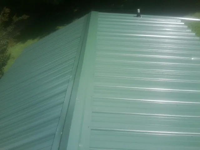 New green metal panels meeting at the ridge of a roof — Flat Roof Repair work by our crew in Laughlintown