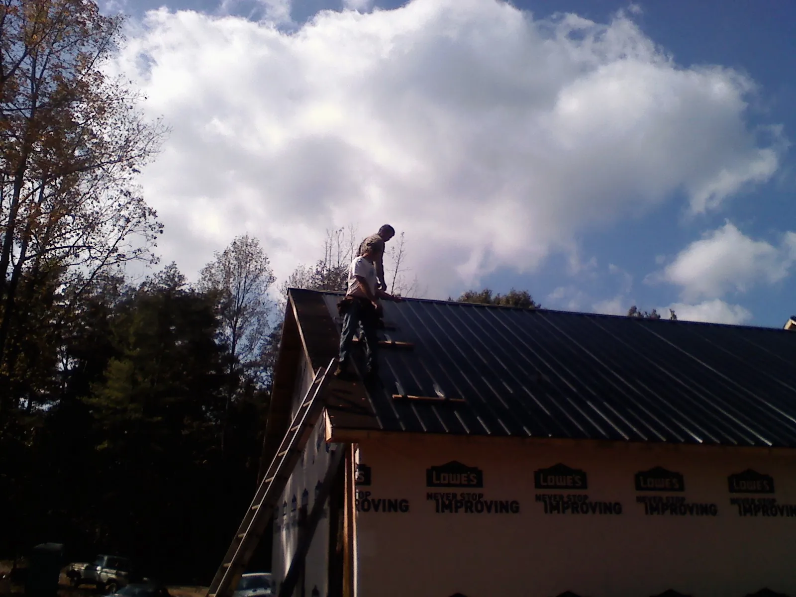 Roofer fastening dark metal panels high against a cloudy sky, from a Roof Inspection job in Laughlintown