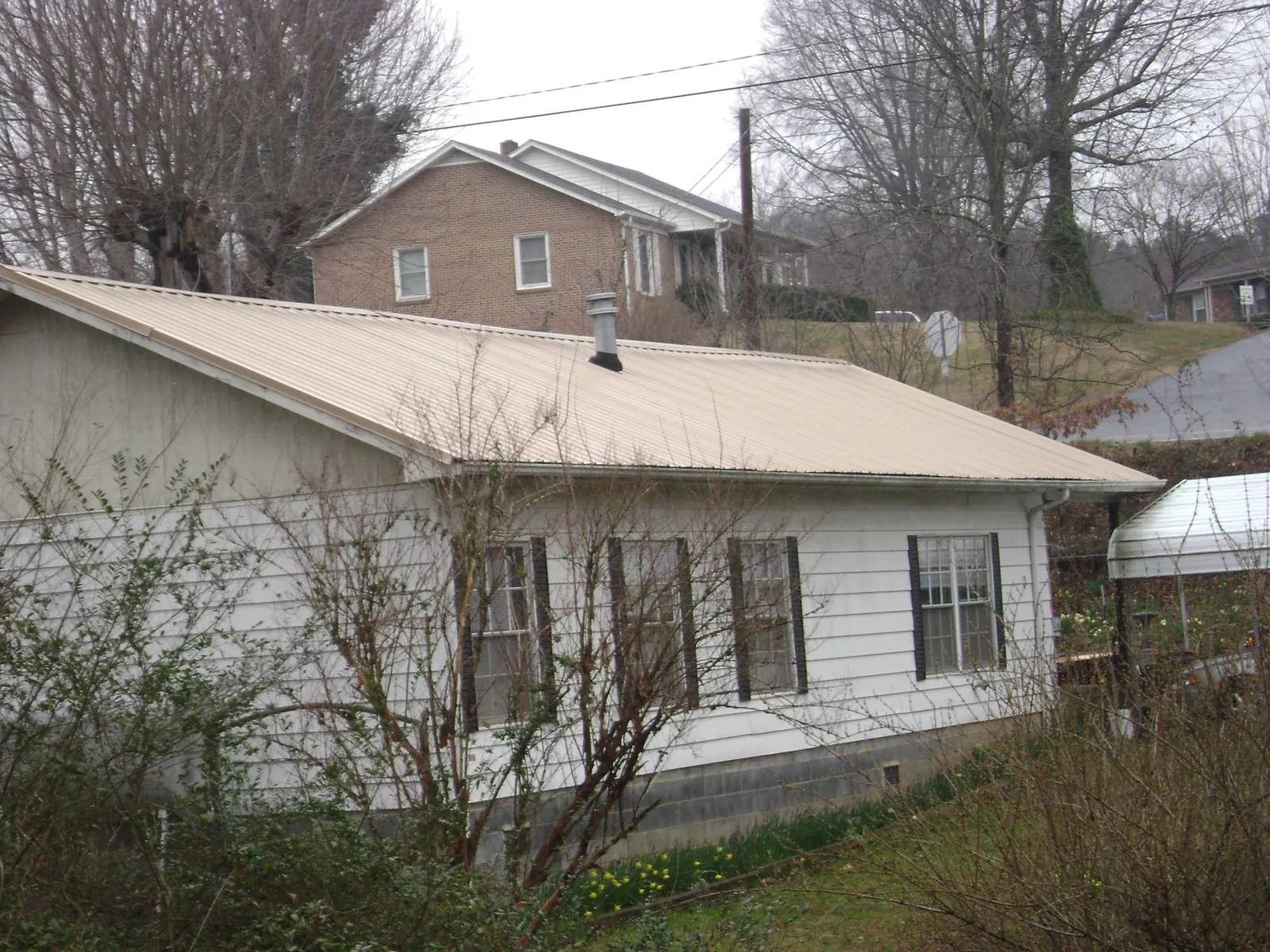 Tan metal roof on a white sided house set into a hillside — Commercial Roofing by Roofing Brothers in Laughlintown