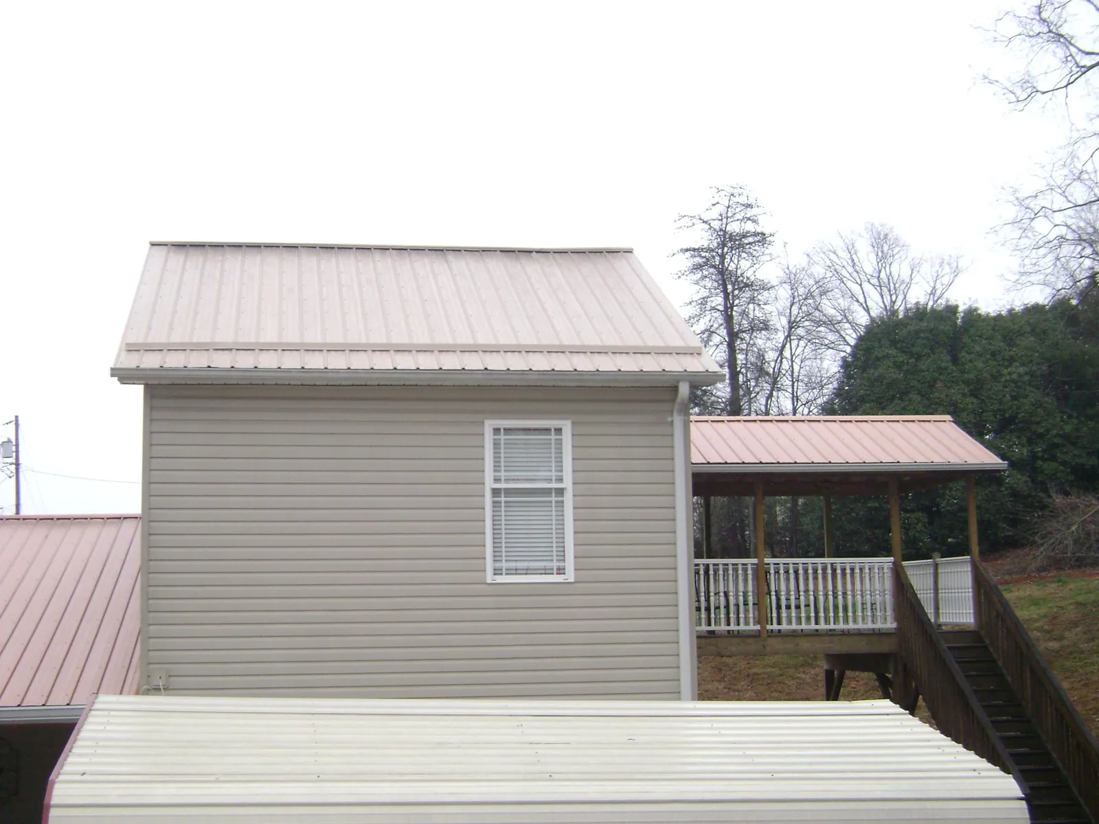 Tan metal roofs on a two story addition and attached porch, from a Roof Replacement job in Laughlintown